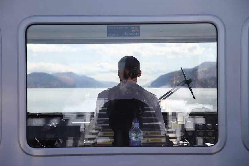 A photo of ship captain taken from behind sitting on his chair facing the windshield.
