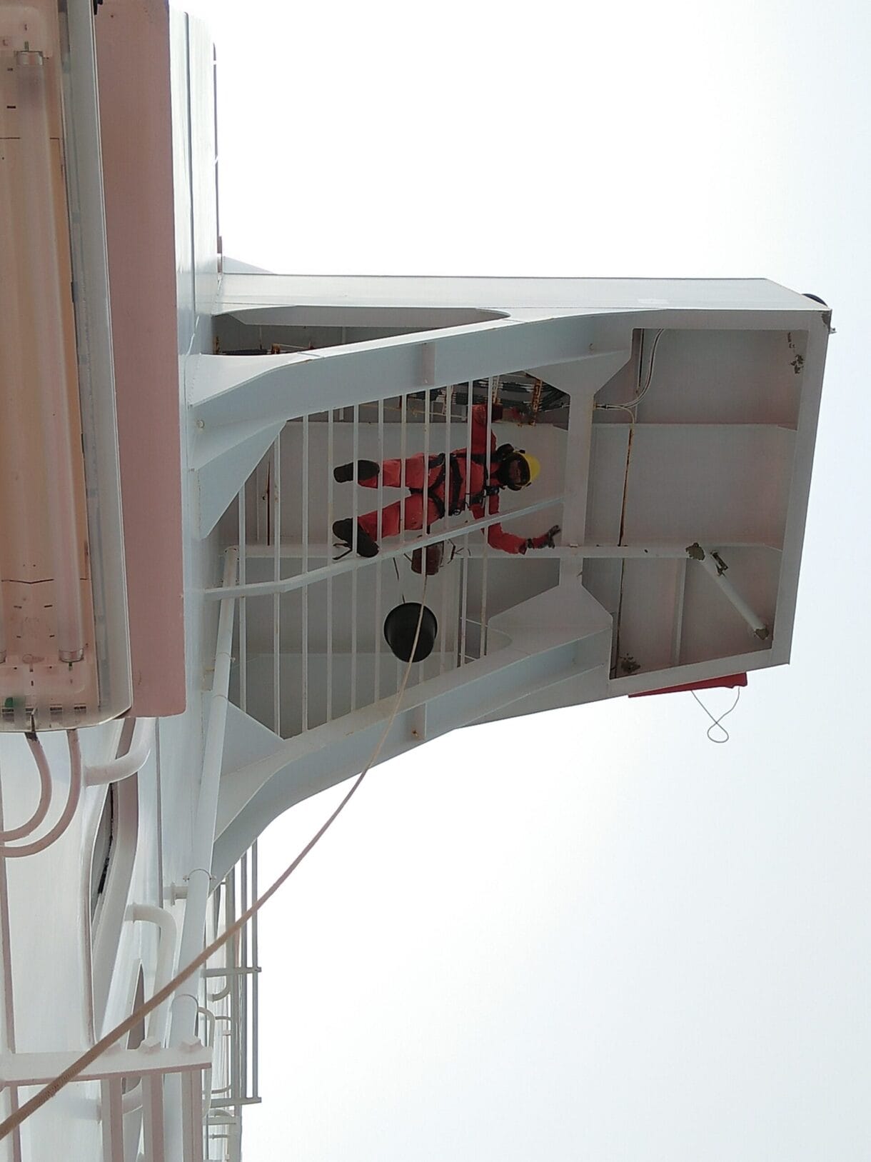 Bosun painting under the starboard bridge wing wearing helmet and safety harness.
