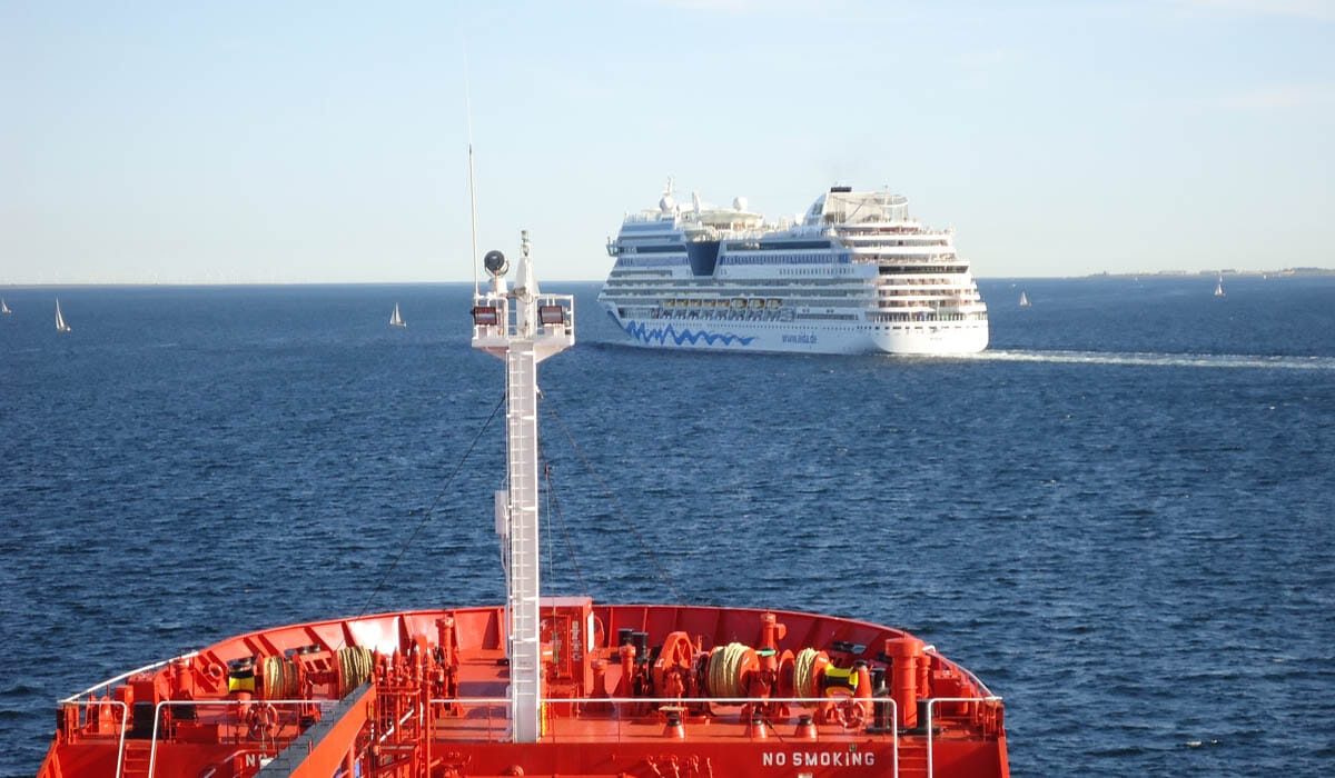 A Passenger vessel passing ahead of a tanker ship while small yachts cruise around the area.