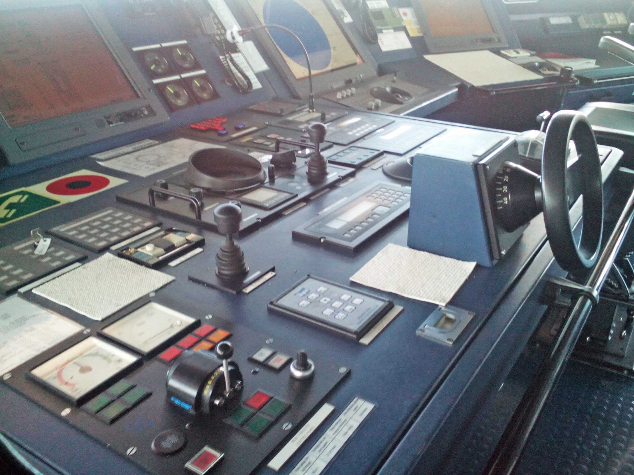 Integrated equipment and control system in the bridge showing various panels and the helm.