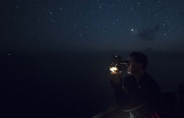 A man taking a sight of a star with his sextant during night time.