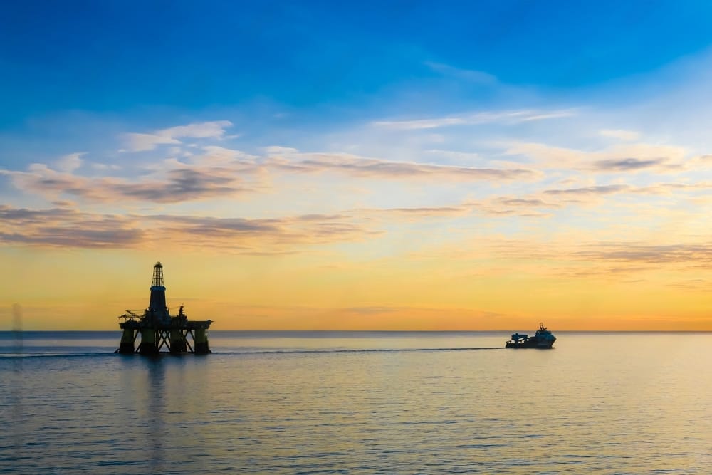 A tugboat towing a huge oil platform on a calm sea.