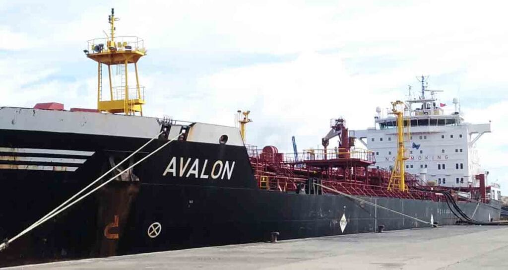 A tanker ship with low freeboard discharging on a flat jetty where the security watchman can view the vessel surroundings with ease.