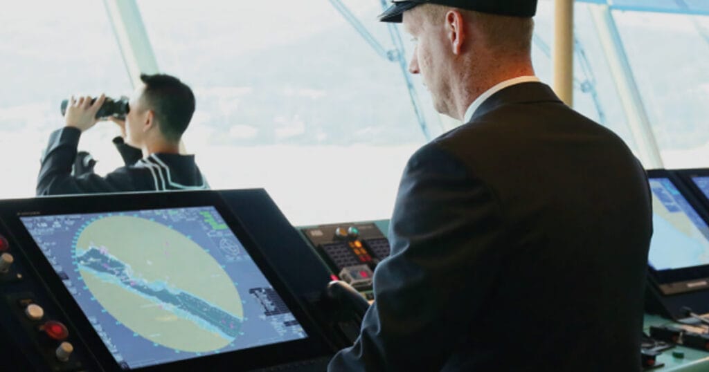 A marine officer looking at the ship's radar while navigating along a narrow channel.