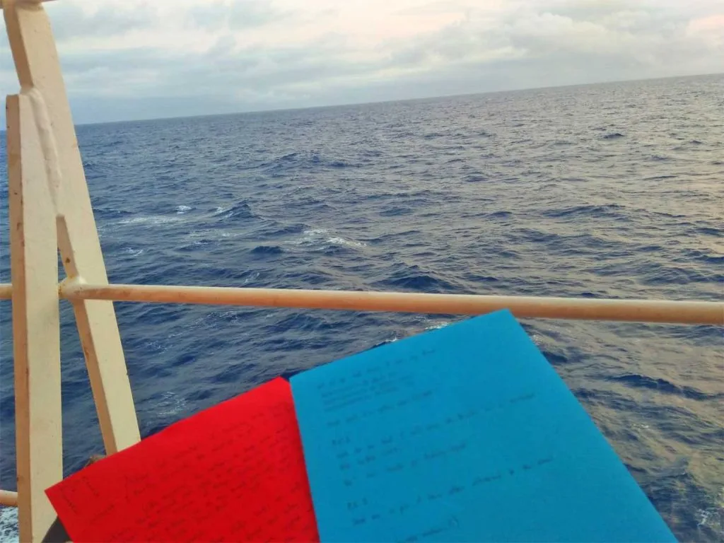 Red and blue paper with written messages with the endless blue ocean in front.
