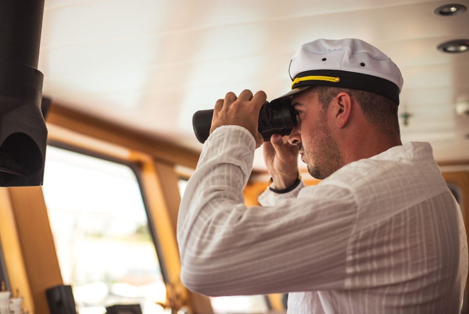 A crew using binoculars to see something outside the bridge window.